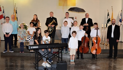Das Foto zeigt die Gruppe der „Jungen Töne“ mit Leon Herget (7. von rechts – mit Mozart-Schirm)  und allen Mitwirkenden: Luca Herget (Klavier), Gabriela Lebiecki (Gesang), Ela Yalcin (Klavier), Marlene Krieg (Gesang und Klarinette), Lara Pothen (Klavier), Jonas Pothen (Klavier), Philipp Schöppner (Tenorhorn), Maximilian Maloney (Klavier), Leon Herget (Klavier und Moderation), Karl Schuldt (Orgel und Klavier), Jakob Drossel (Cello), Elias Drossel (Cello), Karl Schuldt (Orgel und Klavier), Dr. Krystian Skoczowski (Klavierbegleitung für  Gesang und Celli)